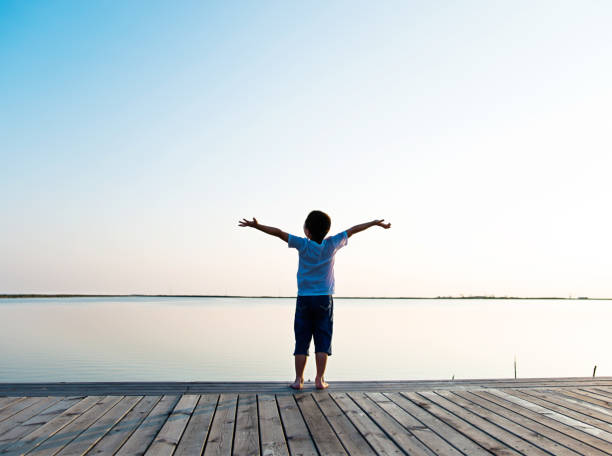 istock Little boy standing at lakeside with arms outstretched 1094476026