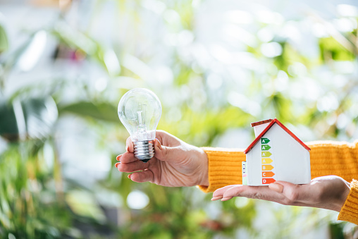 selective focus of led lamp and carton house model in woman hands, energy efficiency at home concept