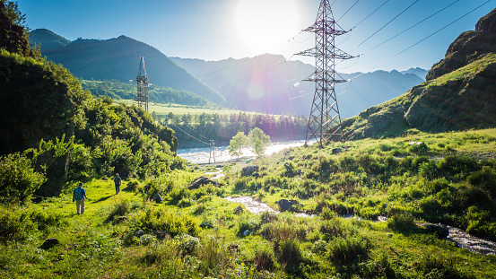 Power lines in the beautiful mountain landscape with a water stream in Altai, Siberia, Russia.
