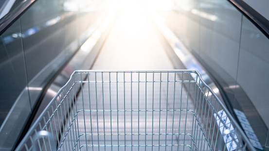 Empty metal shopping cart (trolley) on travelator or escalator in supermarket or grocery store. Shopping lifestyle concept