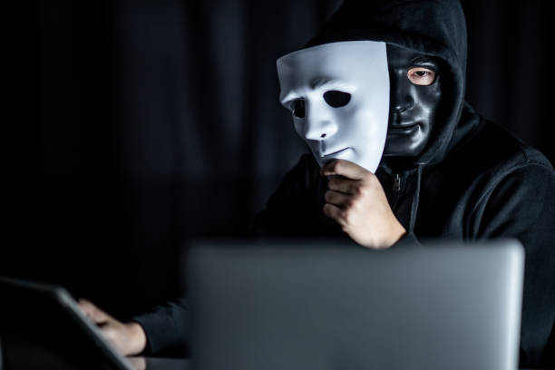 Mystery male hoodie hacker wearing black mask holding white mask with laptop computer on the table. Anonymous social masking. Ransomware cyber attack or internet security concepts Mystery male hoodie hacker wearing black mask holding white mask with laptop computer on the table. Anonymous social masking. Ransomware cyber attack or internet security concepts synthetic identity theft stock pictures, royalty-free photos & images