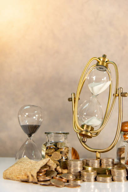 istock Sand running through the shape of hourglass with coins stack and currency jars on table. Time investment. Retirement saving concept. Urgency countdown timer for business payment deadline 1094496988