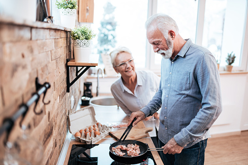 Smiling senior man preparing food for him and his wife in cozy kitchen.