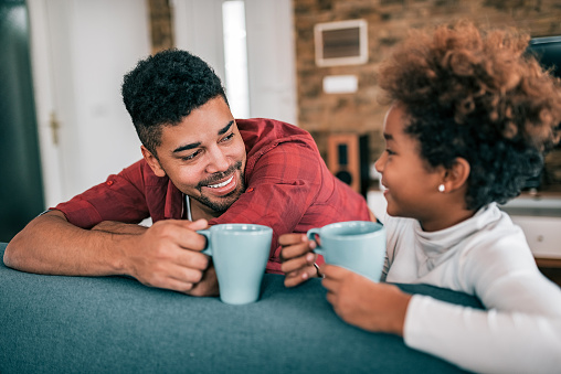 Portrait of a happy young father drinking tea with his daughter at home.