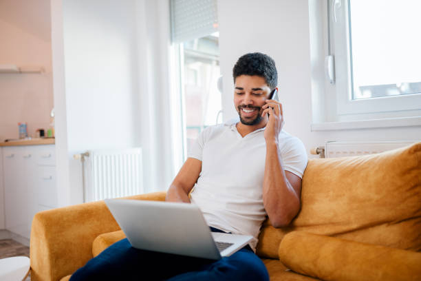 istock Happy african american man talking on smartphone and using laptop at home. 1094499664
