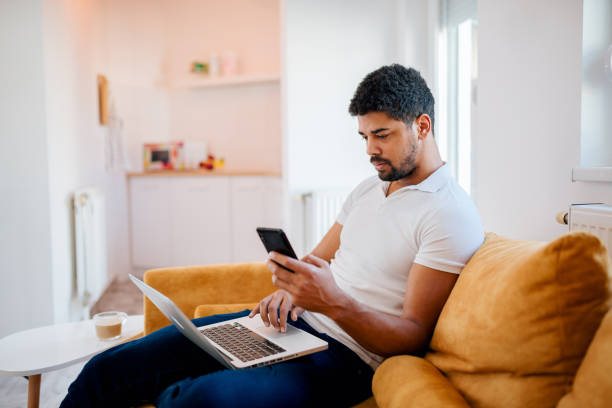 istock Serious young freelancer sitting on sofa with laptop in his lap and using mobile phone. 1094499700