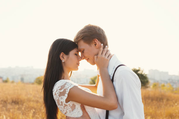 istock Loving couple dressed in white, ready to kiss outdoors with closed eyes while touching faces and foreheads gently 1094499964