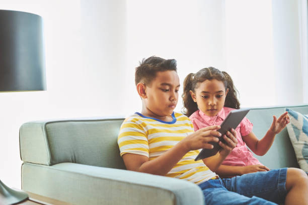 istock Girl sitting by brother using tablet at home 1094503826
