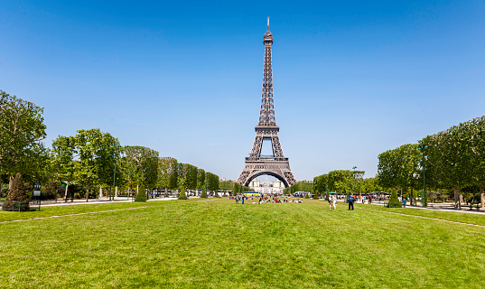 Wide shot of the iconic Eiffel Tower in Paris, France, with tourists and vehicles on a partly cloudy day.