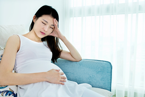 Pregnant woman sitting on sofa and having headache