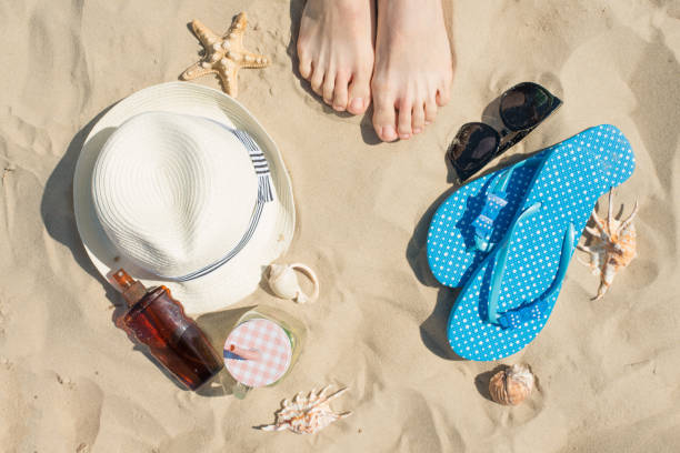 istock Hat, sunscreen, slippers, legs and seashells on sand, top view 1094539156