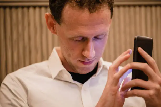 A close-up of a man wearing casual clothing, he has his smartphone in his hand and he is using a visually impaired mobile app to help assist him.