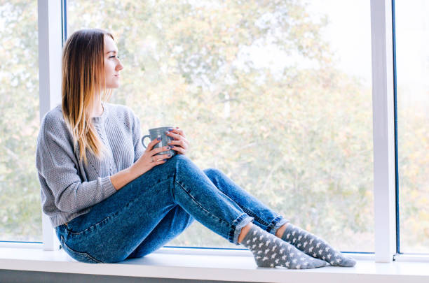 istock A girl sits near a large window and drinks tea. 1094563492