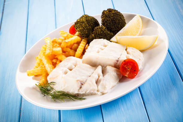 Fish dish - cod with French fries and vegetables on wooden background
