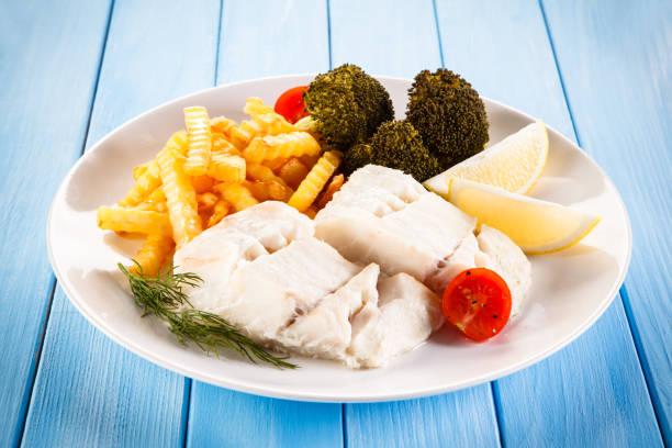 Fish dish - cod with French fries and vegetables on wooden background