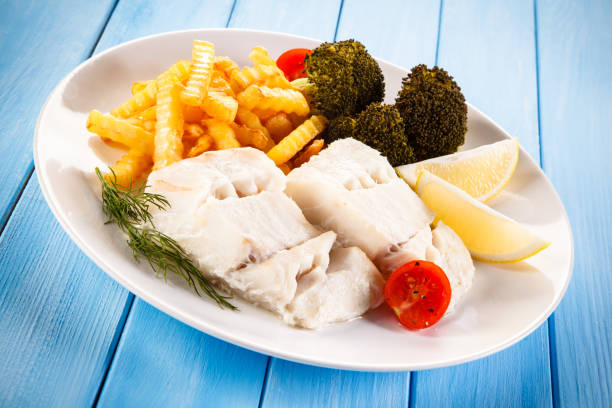 Fish dish - cod with French fries and vegetables on wooden background