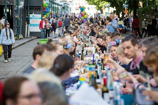 Helsinki, FINLAND - JUNE 12, 2018: Long table with lots of people eating and drinking together. The Day of City Celebration in centre of Helsinki. Finnish your dinner under the sky.