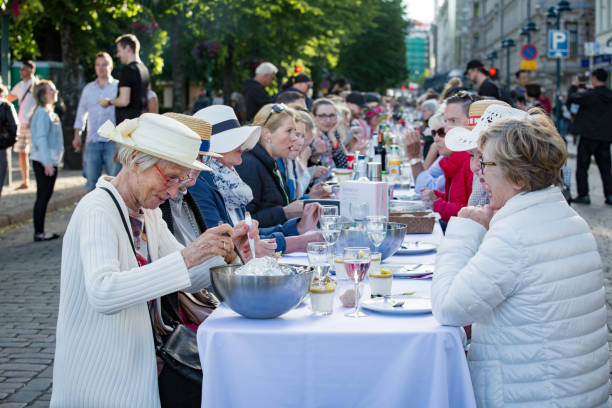 Helsinki, FINLAND - JUNE 12, 2018: Long table with lots of people eating and drinking together. The Day of City Celebration in centre of Helsinki. Finnish your dinner under the sky.