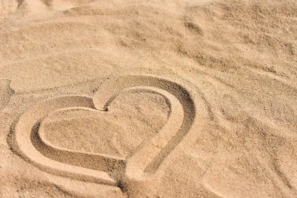 Photo of Hand drawn heart on sea sand on the beach