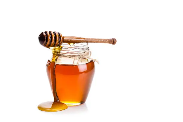 Open honey jar with a honey dipper dripping honey on the jar and table. The composition is isolated on white background at the left of an horizontal frame leaving useful copy space for text and/or logo. High key DSRL studio photo taken with Canon EOS 5D Mk II and Canon EF 70-200mm f/2.8L IS II USM Telephoto Zoom Lens