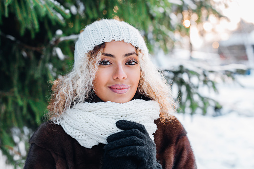 Outdoor close up portrait of young beautiful girl with afro hair in winter forest . Christmas, winter holidays concept. Snowfall.
