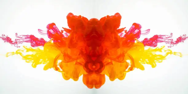 Movement of acrylic colours in water photographed while in motion. Abstract swirling of ink in water. Splash of ink isolated on white background. Yellow-red acrylic colour dissipation