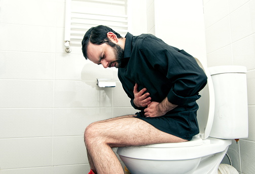 Vista lateral del hombre que sufre de dolor de estómago sentado en el asiento del inodoro photo
