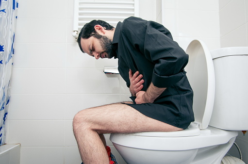 Vista lateral del hombre que sufre de dolor de estómago sentado en el asiento del inodoro photo