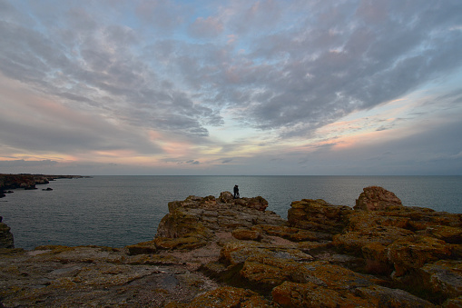 Distant silhouettes of a couple standing on the cliffs high above the see after sunset enjoying the magical moment of romantic love. Black Sea coast near Tyulenovo, Bulgaria