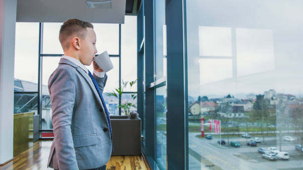 istock Boy drinking from mug and looking through window in office 1094611546