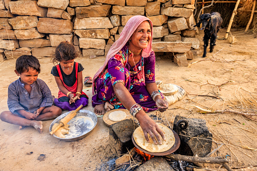 Indian woman preparing food - chapati, flatbread, desert village, India. Her children are waiting for breakfast just next to her
