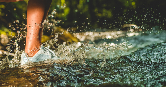 Close-up shot of the foot of a person in a sports shoe running through a stream