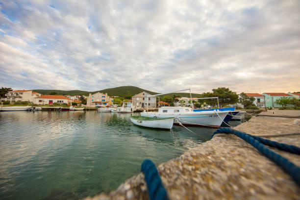 Clouds over white boats moored in village marina with houses in background