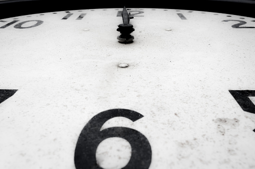 A macro-photograph of part of the face of an antique analogue clock that was manufactured in the United States by General Electric.    Known as the Telechron Clock, (1940) GE marketed this design under the strap line 'as silent as moonlight'.  It was commonly used in institutional settings.  The clock face indicates that it is also 12 o'clock.  Selective focus.  Belfast, Northern Ireland.