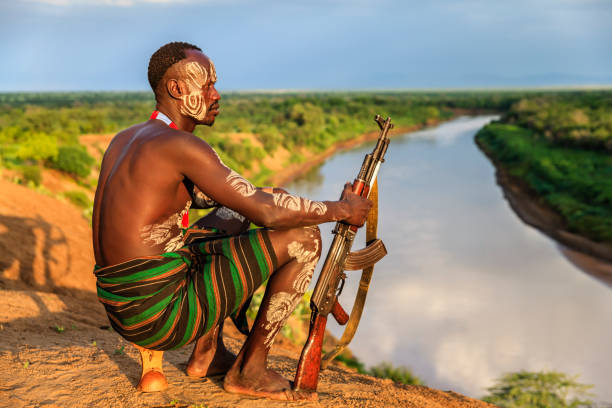 Young African man from Karo tribe posing with AK-47 / Kalashnikov - Ethiopia, East Africa. The Karo tribe is a tribe that lives in the southwestern region of the Omo Valley near Kenya, Africa. They are largely pastoralists.