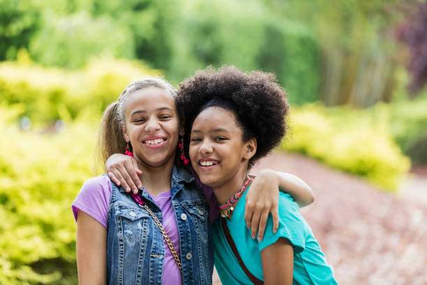 Two girls, elementary & pre teen, are sitting on stairs and talking to each other.  Nature body shot.