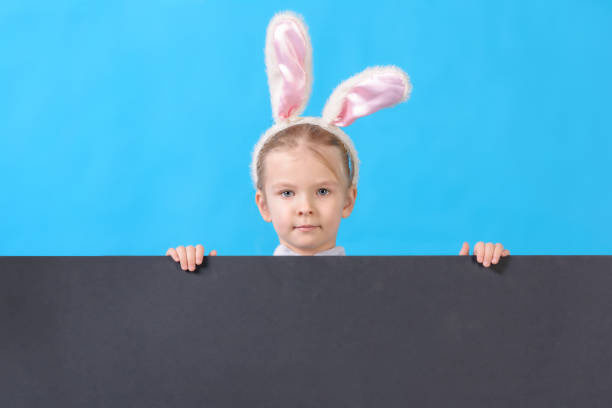 istock Little girl in a white Easter bunny costume. Bottom empty space on a black background. Bright layout with copy space. 1094649136
