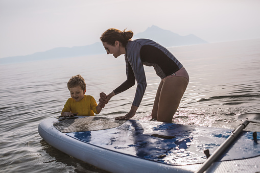 Mother and son having fun with paddle board in the sea.