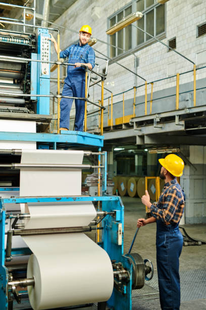 istock Content industrial employees in hardhats working on printing press and talking during production process 1094663002