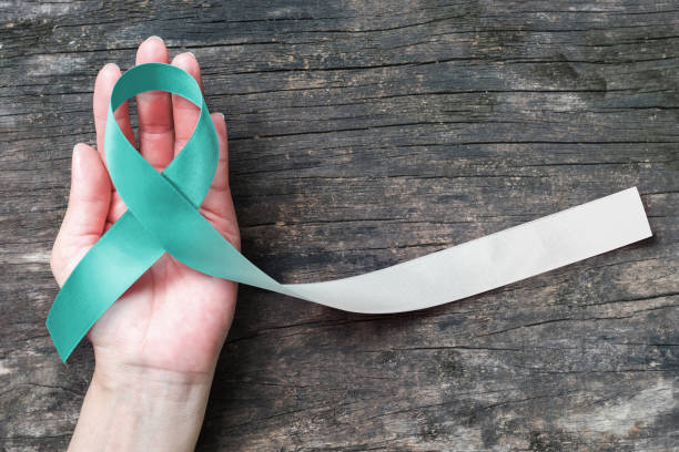 Teal and white ribbon for Cervical Cancer awareness campaign concept symbolic bow color on woman helping hand support on old aged wood Teal and white ribbon for Cervical Cancer awareness campaign concept symbolic bow color on woman helping hand support on old aged wood cervical cancer photos stock pictures, royalty-free photos & images
