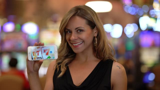 Beautiful latin american woman at the casino holding a smartphone showing lucky 777 on screen