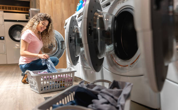 istock Beautiful young woman at a self service laundry loading the washing machine with her clothes while smiling 1094713432