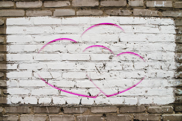 istock Two drawn hearts on brick wall with white paint close-up. Mock up. Urban background with two painted hearts. Imperfect exterior with love symbol graffiti. Valentine day image. Unideal brickwork. 1094713946