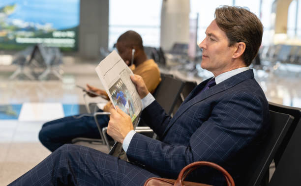 Traveling business man waiting by the gate at the airport and reading the newspaper Portrait of a traveling business man waiting by the gate at the airport and reading the newspaper - travel concepts newspaper airport reading business person stock pictures, royalty-free photos & images