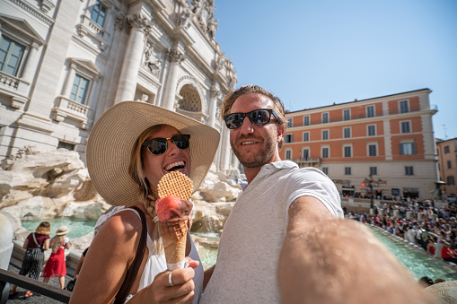 Cheerful couple enjoying Italian vacations in Rome eating gelato ice cream at the Piazza di Trevi fountain