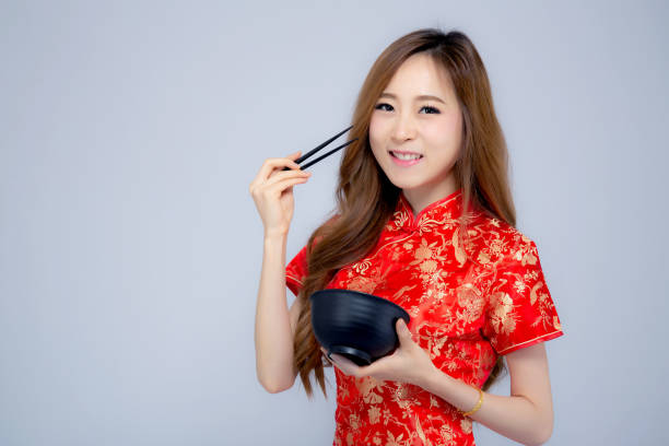 jovem mulher asiática retrato bonito vestir vermelho cheongsam segurando os pauzinhos e tigela isolado no fundo branco, conceito de feriado do ano novo chinês. - chopsticks human hand women isolated - fotografias e filmes do acervo