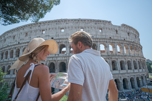 Young couple in Rome at the Colosseum looking at tourist city map for directions; People travel capital cities of Europe concept