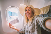 Young woman in airplane takes mobile phone selfie portrait during flight