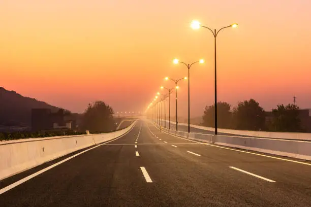 Empty city road and bright street lights landscape at sunset