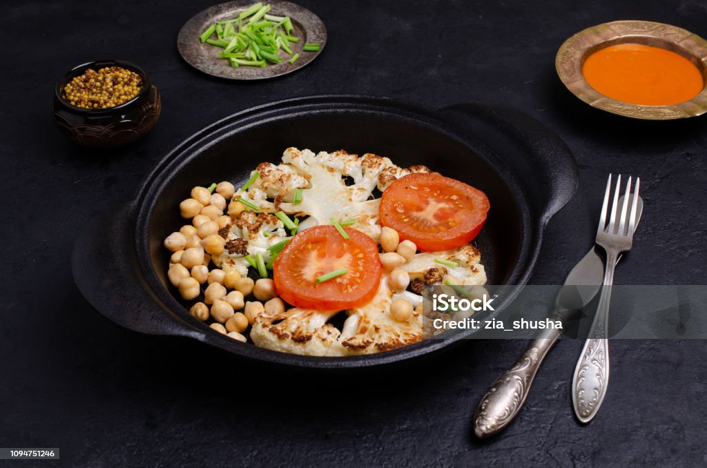 Roast cauliflower steak Roast cauliflower steak with tomatoes and chickpeas. Selective focus. Backgrounds Stock Photo